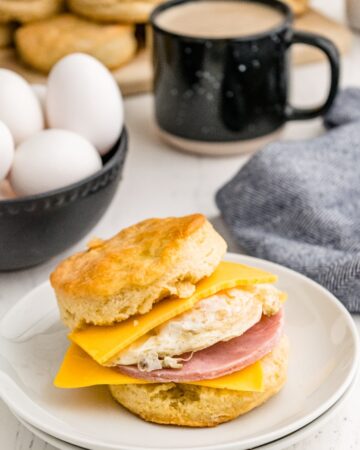 Biscuit sandwich on a white plate filled with egg, ham and cheese.