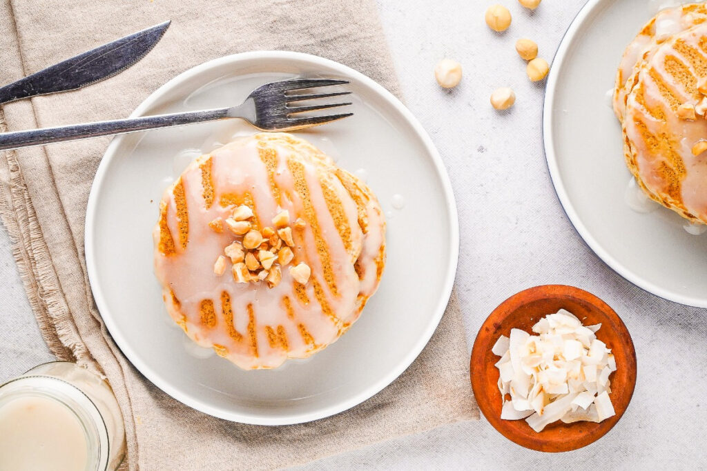 Two plates filled with macadamia nut pancakes topped with coconut syrup. 