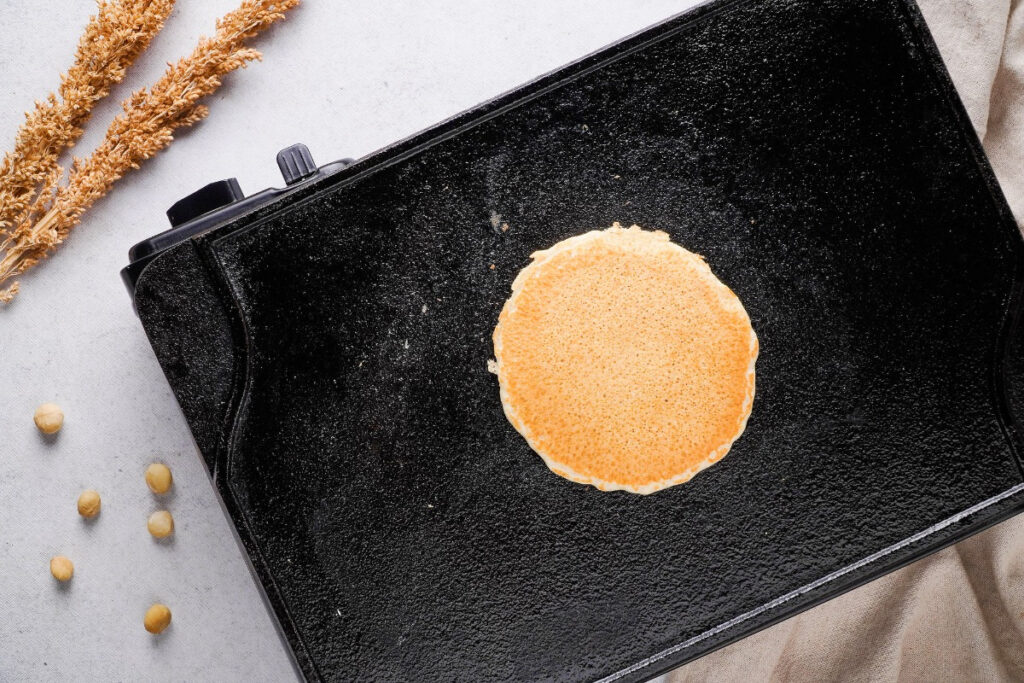 A pancake on a griddle finishing cooking. 