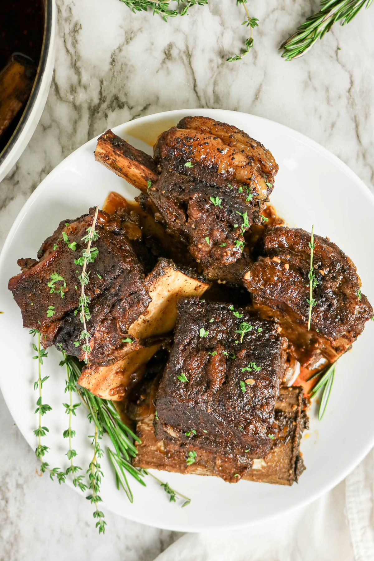 Top overhead view of beef ribs on a white serving plate topped with thyme.
