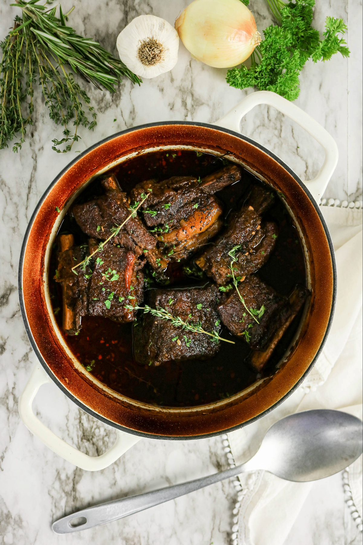Cooked beef short ribs with herbs and a serving spoon on the side of the pot.