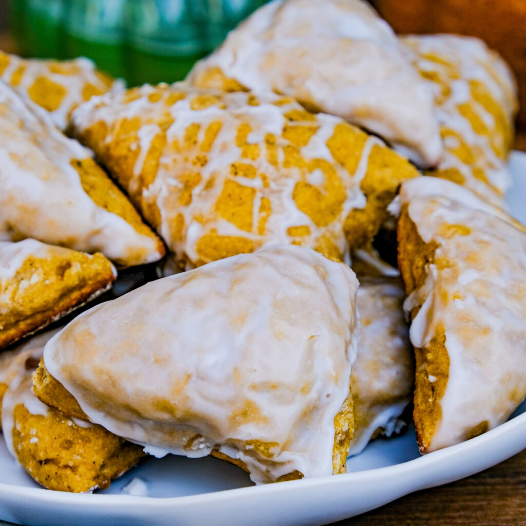 Healthy pumpkin scones made with yogurt topped with a light glaze on a white plate.