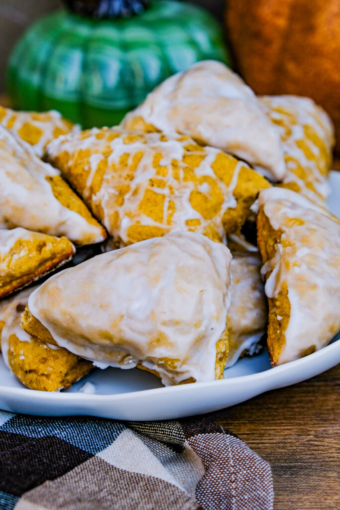 A white plate stacked with pumpkin scones with a sugar glaze. 