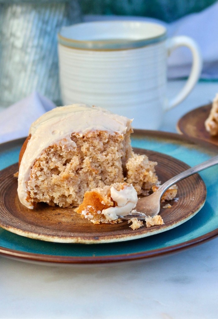 A large slice of spice cake topped with icing with a fork being eaten. 