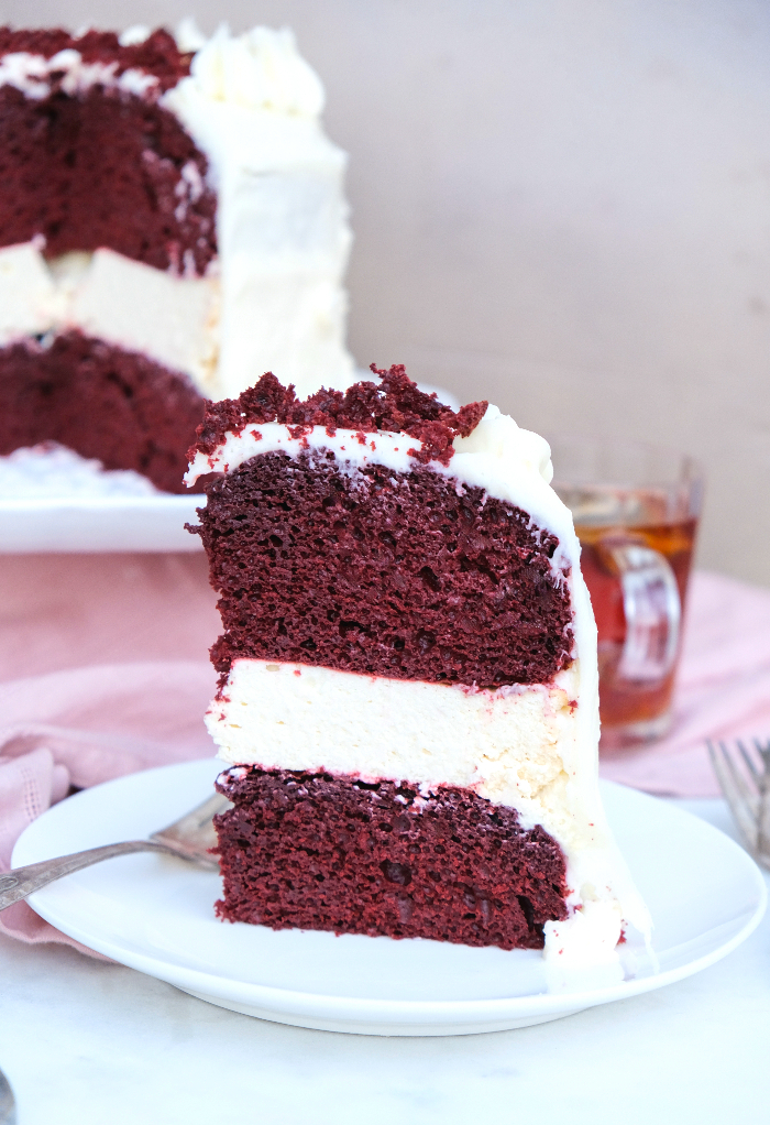 A slice of red velvet cheesecake cake on a white plate. 