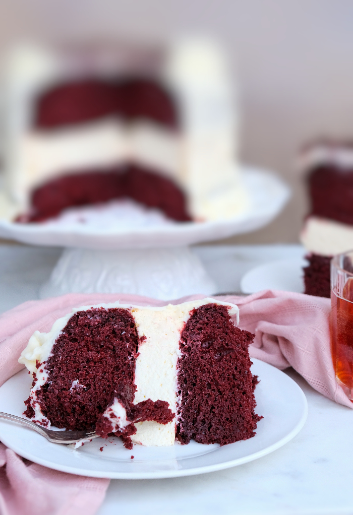A slice of a three layered cake on a white plate with a full cake in the background.