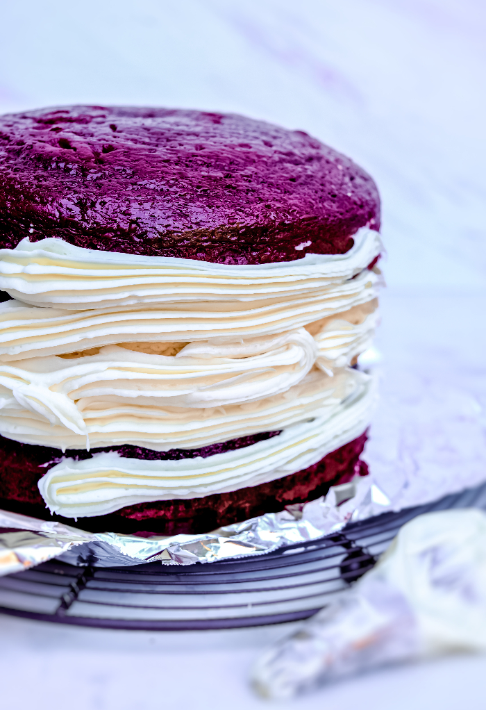 Piping cream cheese frosting on the side of a cake.