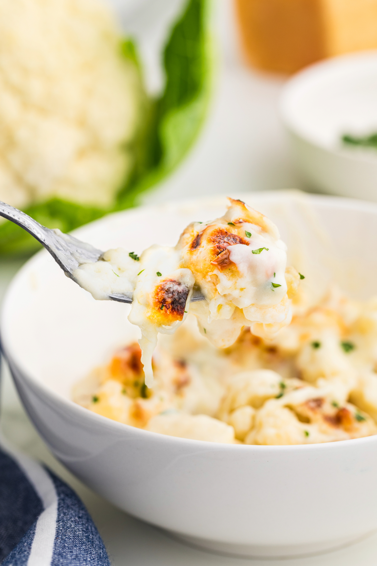 A forkful of cheesy cauliflower casserole in a white bowl.
