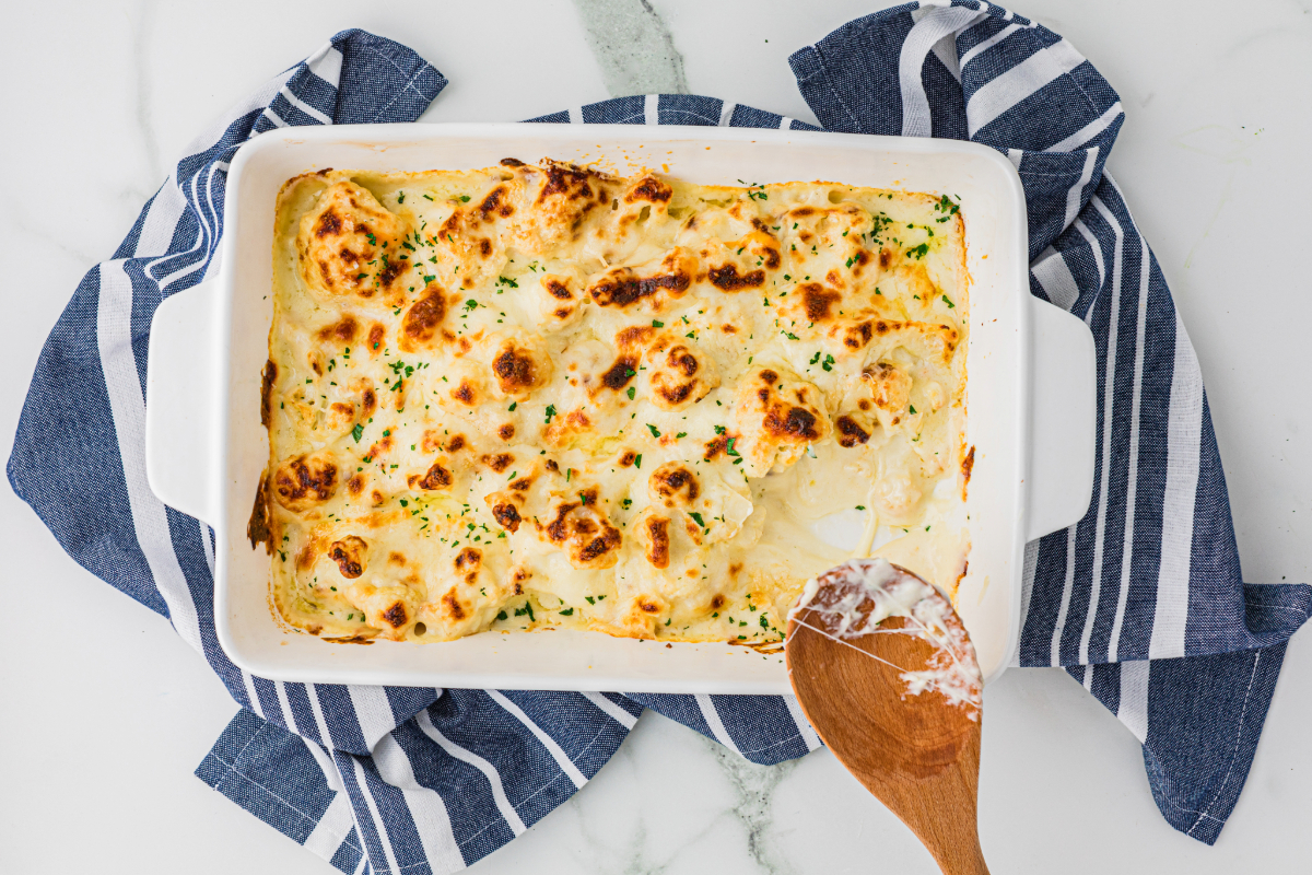 Keto cauliflower casserole in a white serving dish on a blue dish towel.