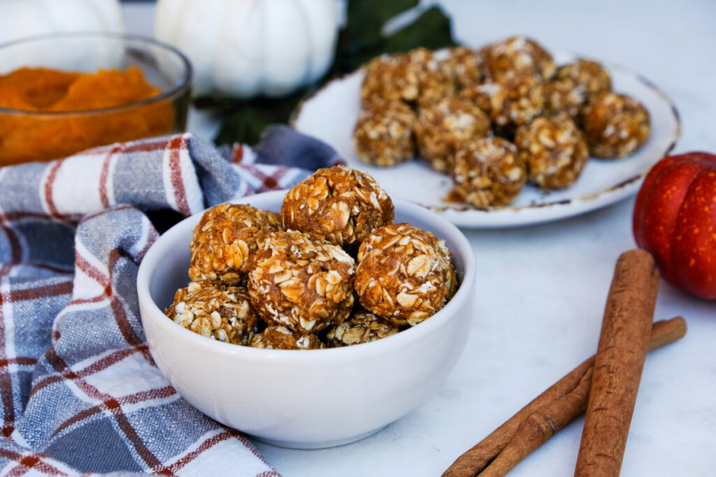 Homemade pumpkin protein bites in a white bowl with cinnamon sticks on the side. 