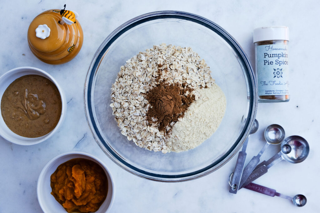 Oatmeal, protein powder, and pumpkin pie spice in a clear mixing bowl. 