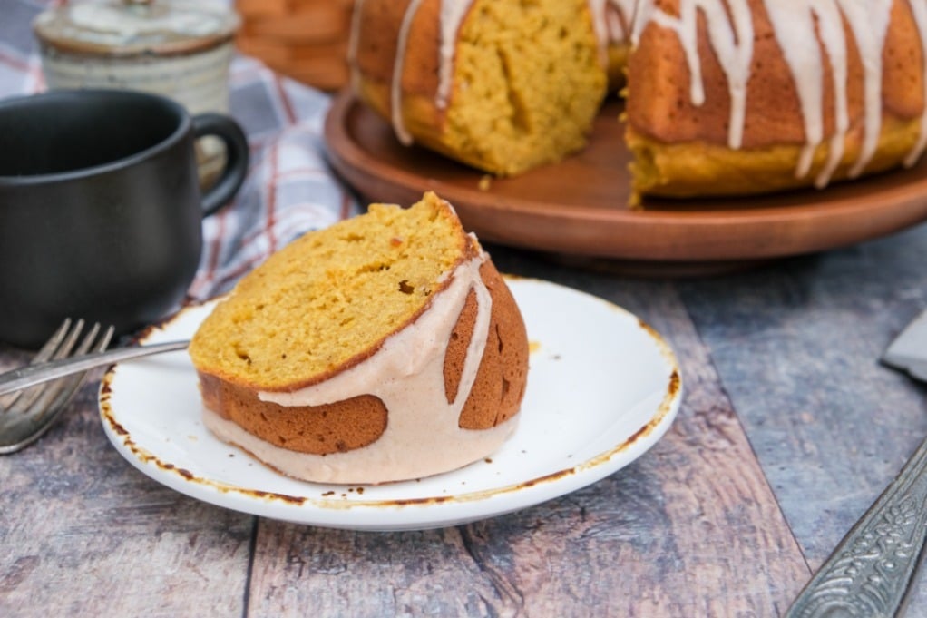 A cake on a a wood serving dish with a slice on a white plate. 