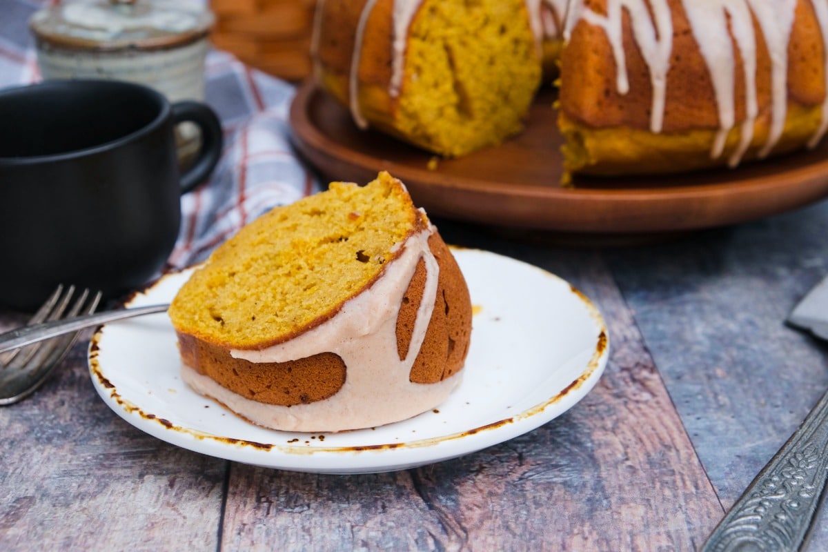 A slice of pumpkin bundt cake on a white plate with a whole cake in the background.