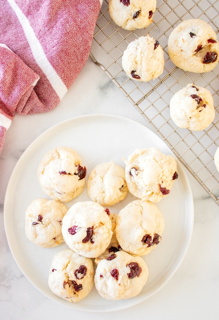 Top view of cookies on a white plate and cookies cooling on a baking rack. 