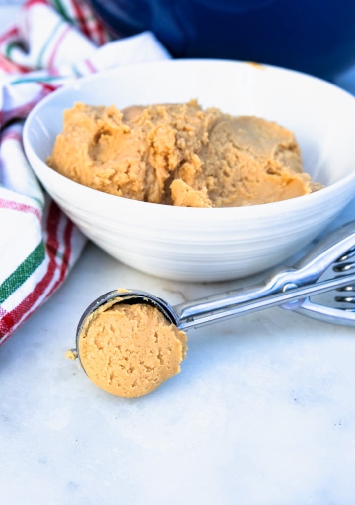 Peanut butter mix in a white bowl with a cookie scoop on the side.