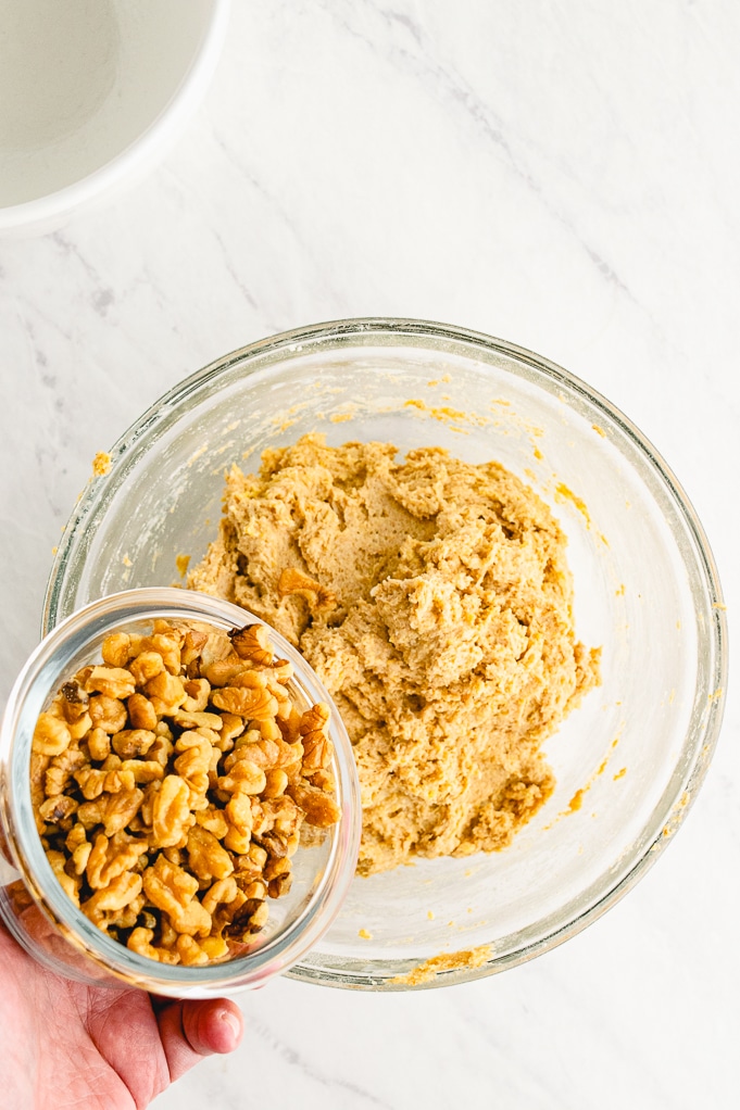 Cookie dough mixed with walnuts in a clear bowl.