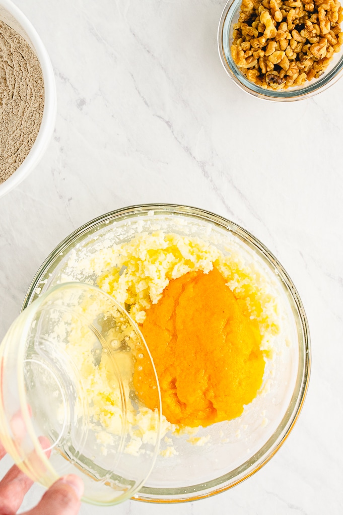 Persimmon pulp added to butter mix in a clear mixing bowl.