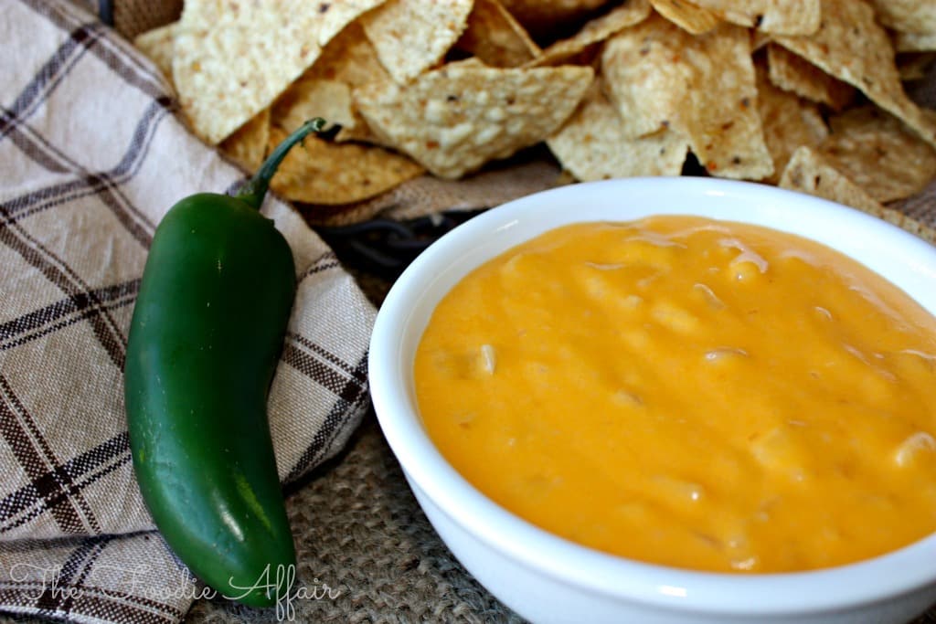 creamy nacho cheese sauce in a white bowl with a jalapeno on the side. 