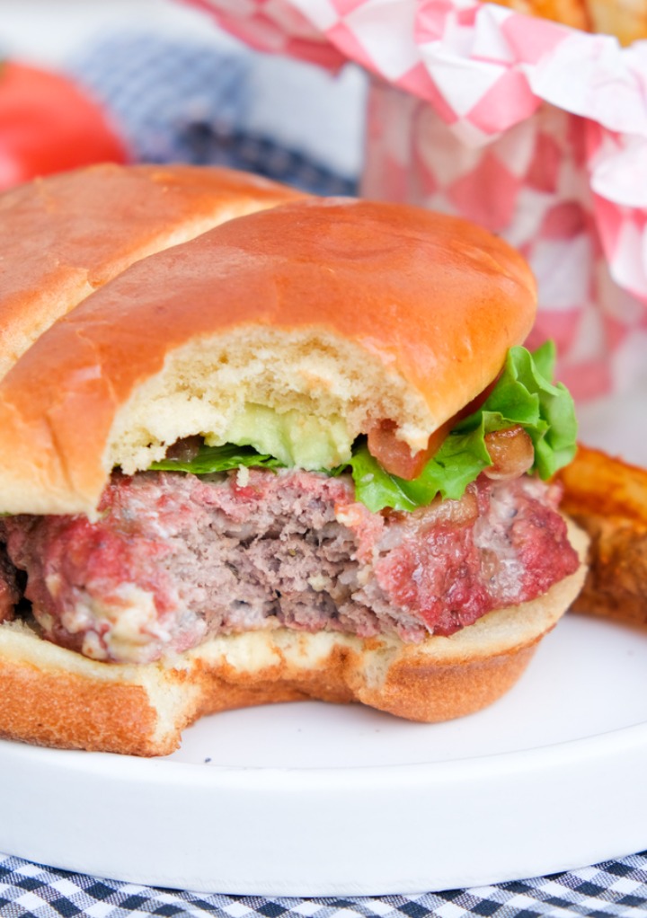 A burger on a white dish with a bite taken out of it. 