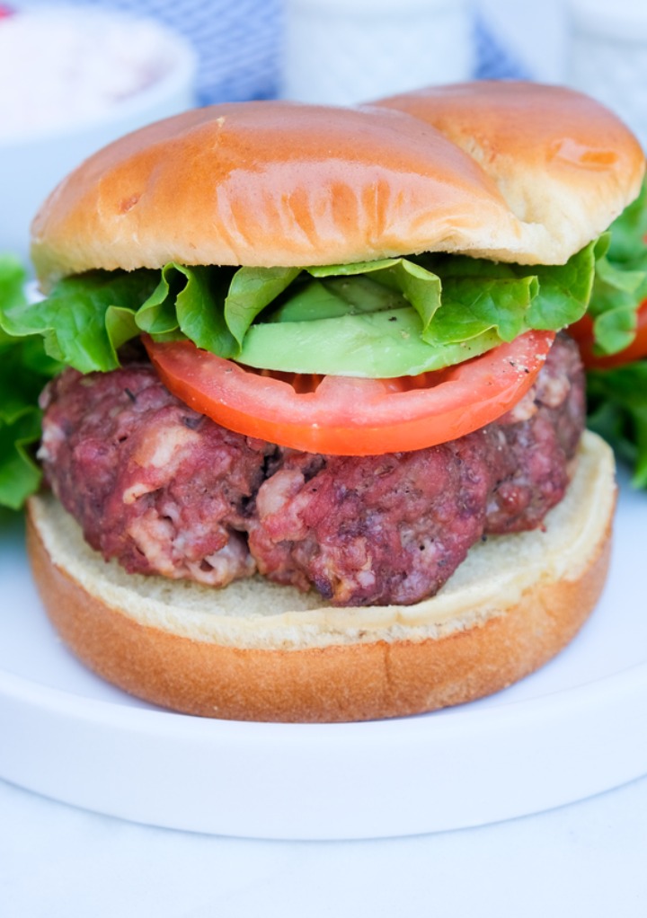 A hamburger with tomato and lettuce on a white plate ready to eat. 