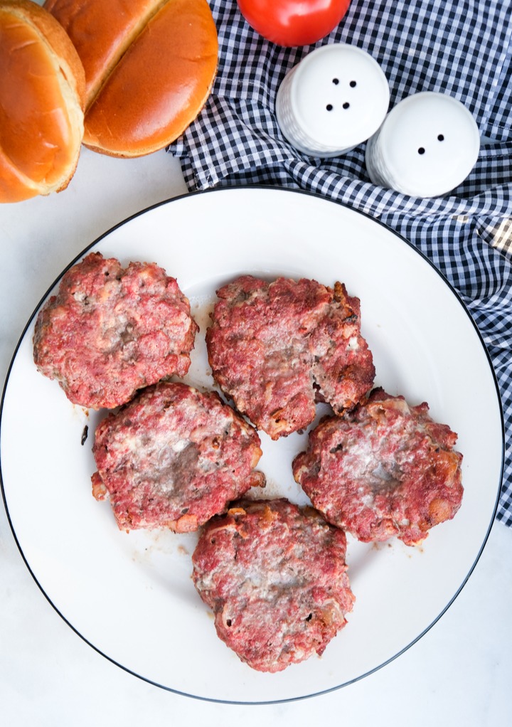 Cooked hamburgers on a white plate ready to assemble.