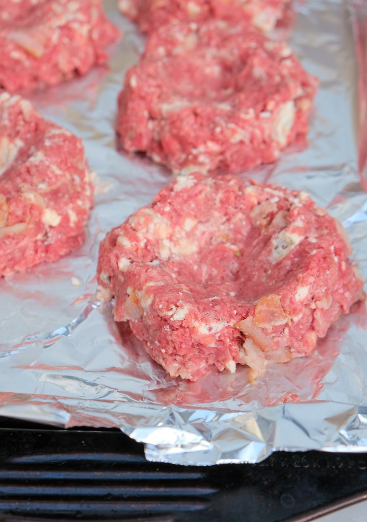 Raw hamburgers formed and placed on a foil lined baking sheet before cooking. 