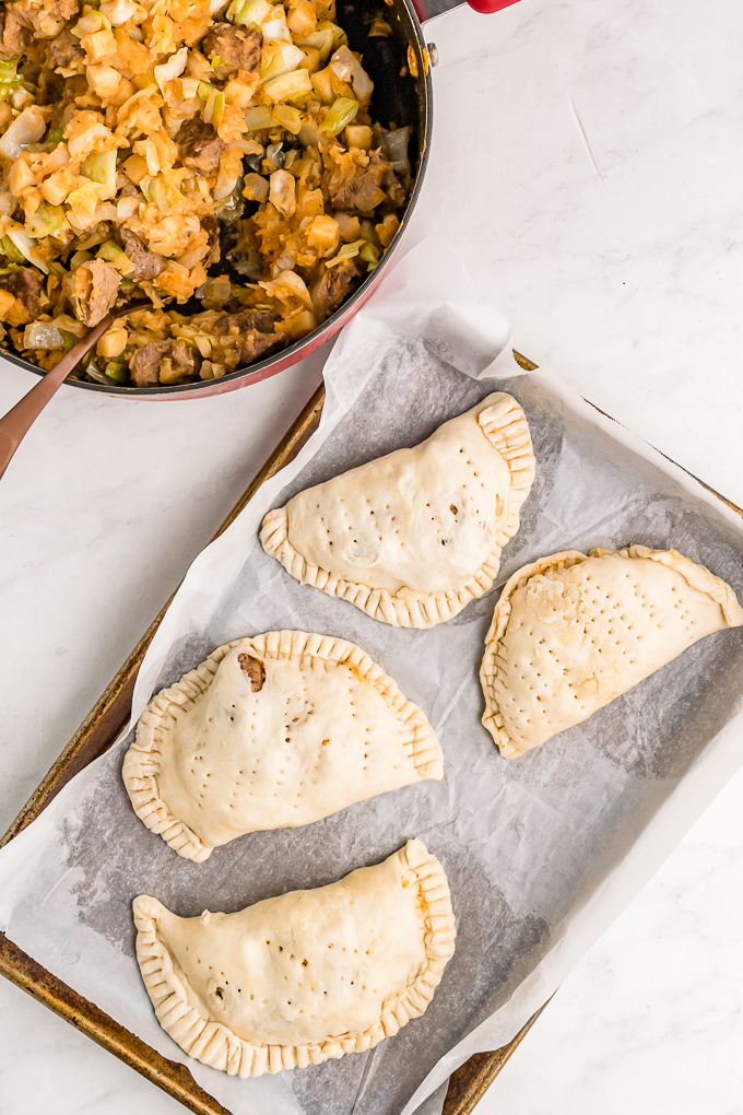 A baking sheet with savory meat pies ready to bake.