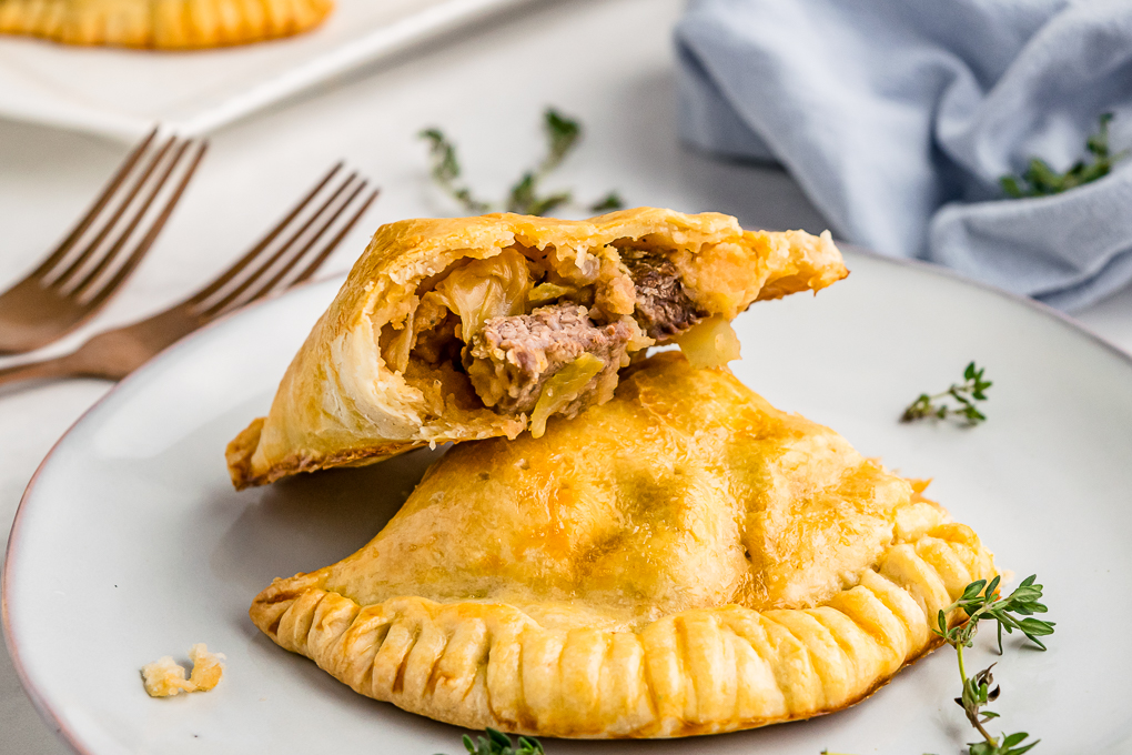 Baked savory meat hand pies on a white plate partially eaten. 