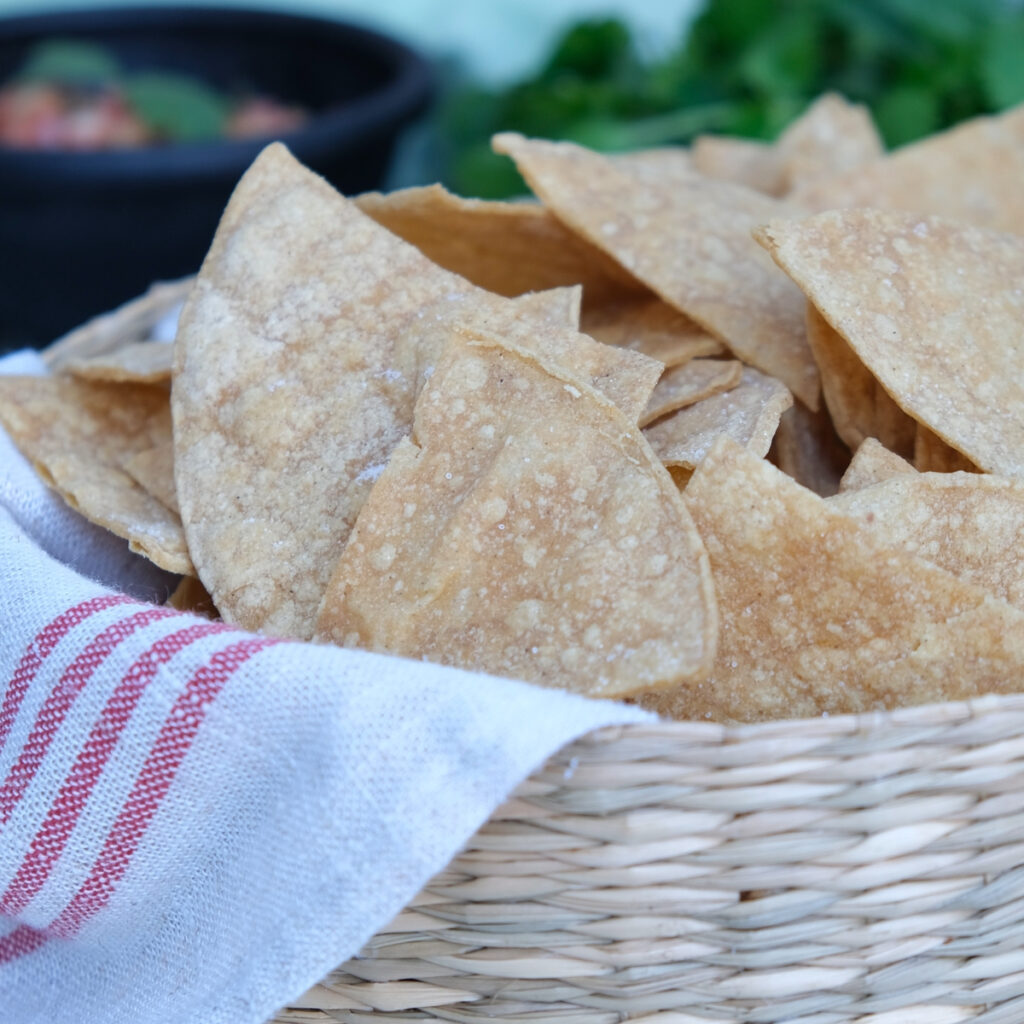 Homemade baked tortilla chips in a straw basket.