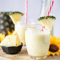 Clear glass filled with pineapple smoothie with a red straw.