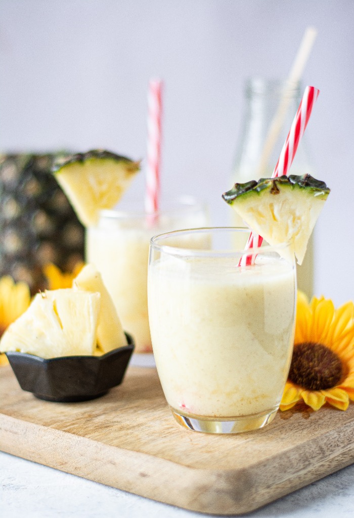 Clear glass filled with pineapple smoothie with a red straw.
