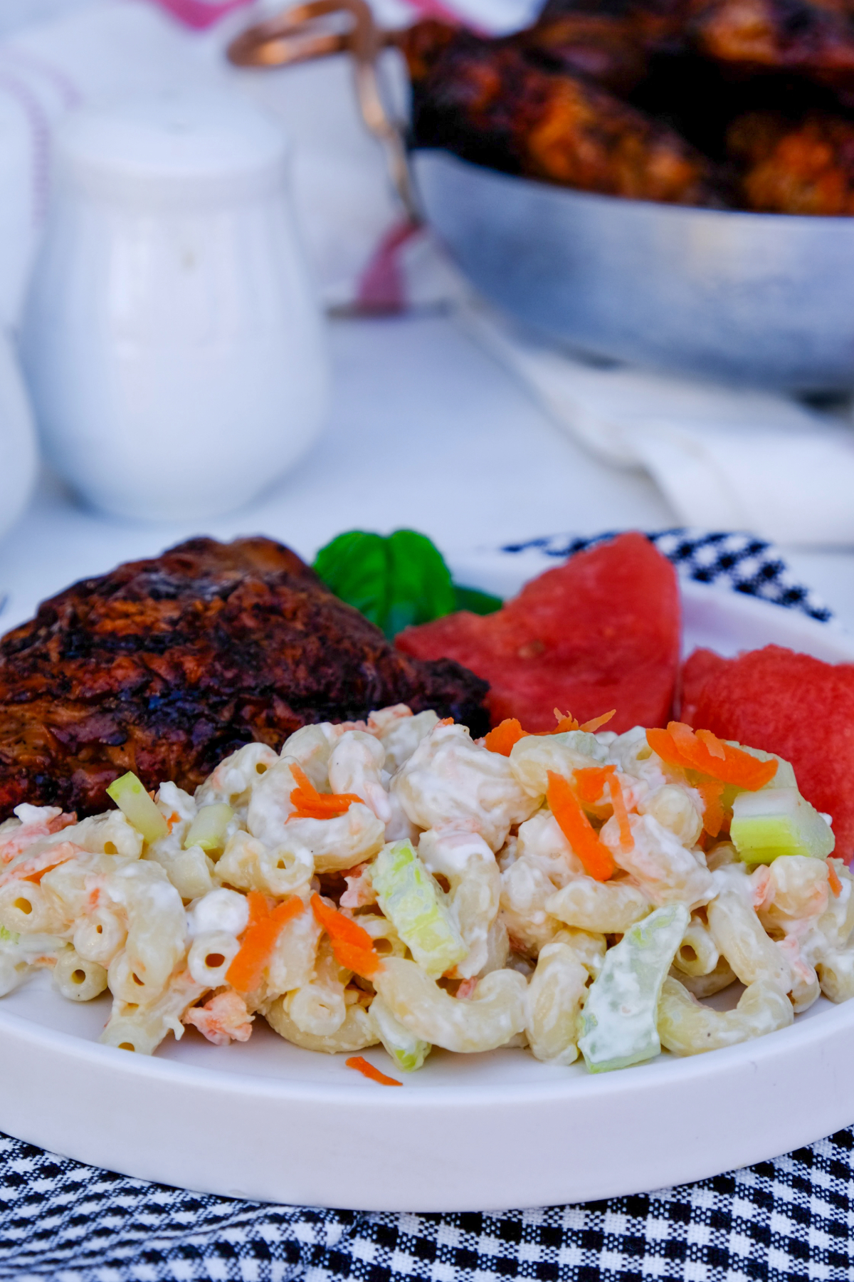 Plate lunch of chicken, watermelon, and Hawaiian macaroni salad on a white serving plate. 
