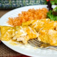 Homemade enchiladas with green sauce on a white plate with Spanish rice.