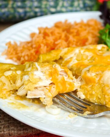 Homemade enchiladas with green sauce on a white plate with Spanish rice.