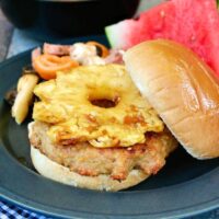 Teriyaki Burger topped with grilled pineapple on a black plate.