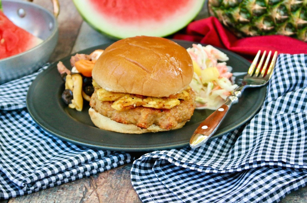 Black plate with a turkey burger, coleslaw and watermelon. 