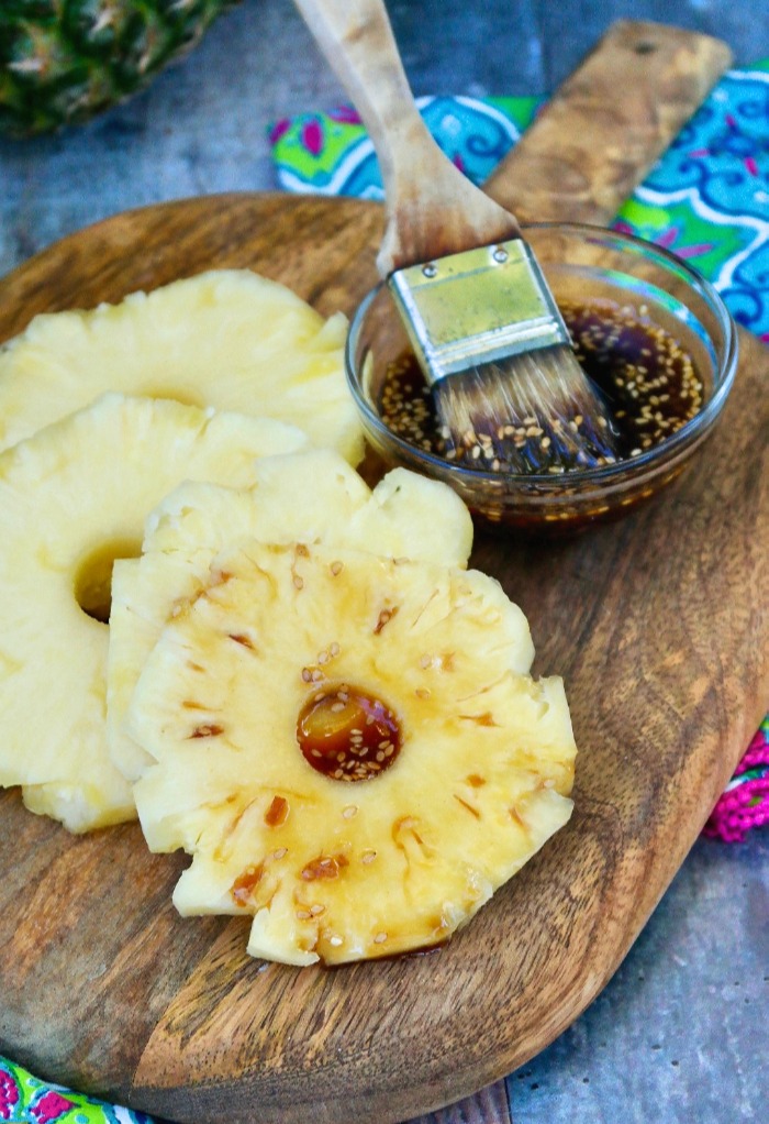Sliced pineapple topped with teriyaki sauce for grilling.