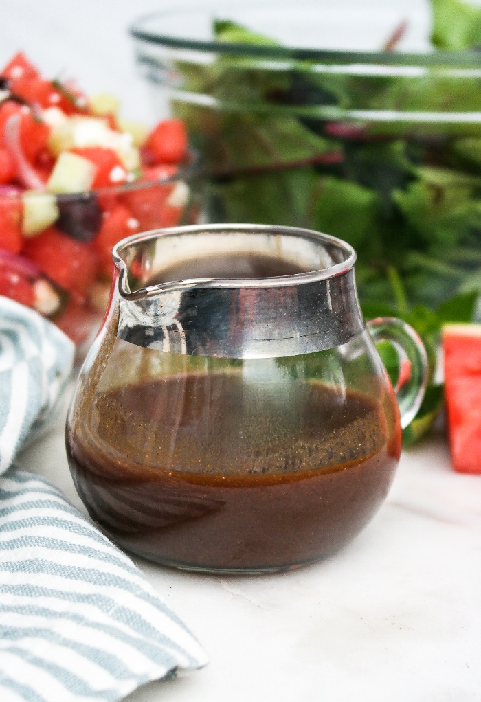 Dijon balsamic salad dressing in a small clear pitcher with a silver rim. 