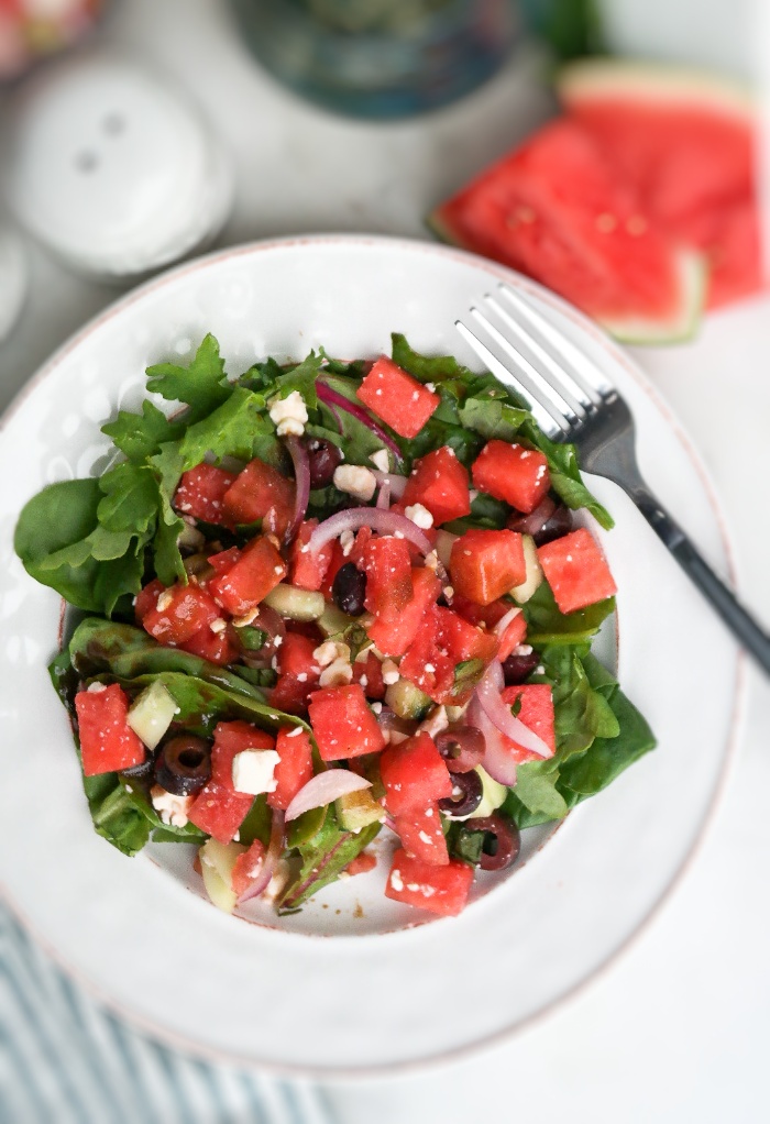 White salad plate topped with salad and watermelon. 