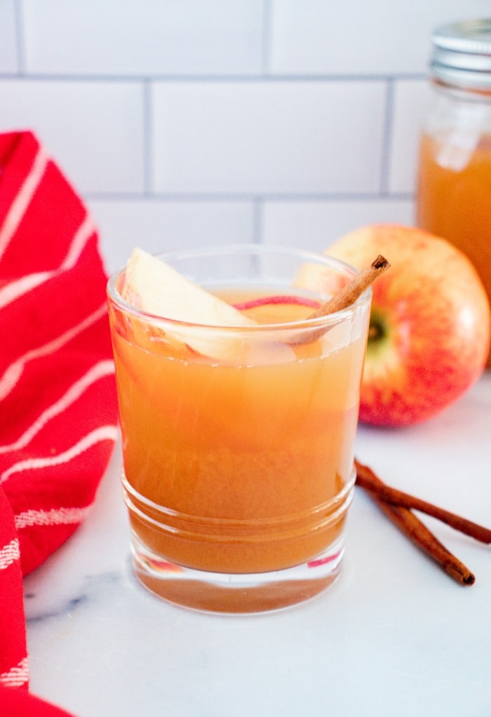 A glass filled with apple pie moonshine with a slice of apple and cinnamon stick. 