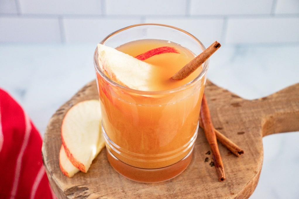 A clear glass of apple pie moonshine cocktail on a wooden trivet.