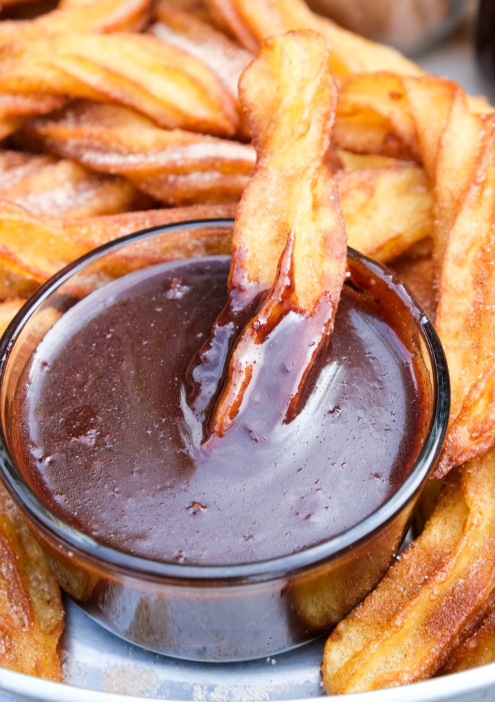 chocolate sauce in a clear small bowl with a mini churro dipped in the sauce. 