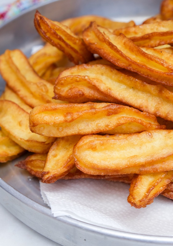 Fried churros on a paper towel lined stainless steel plate. 