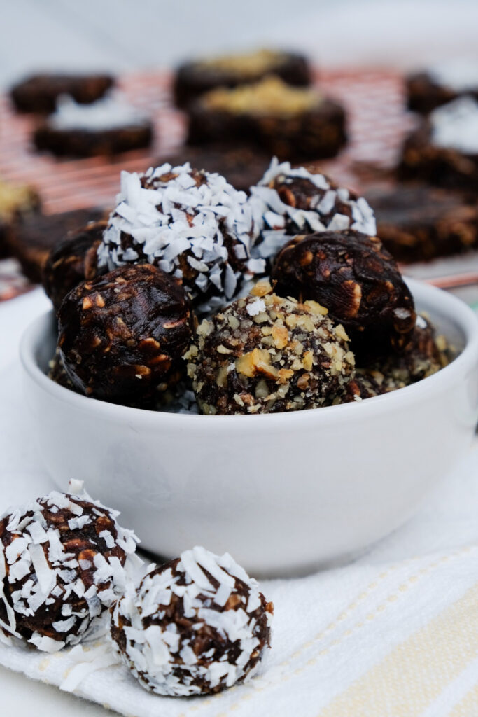 no bake cookie balls rolled in coconut flakes and chopped nuts in a small white bowl. 