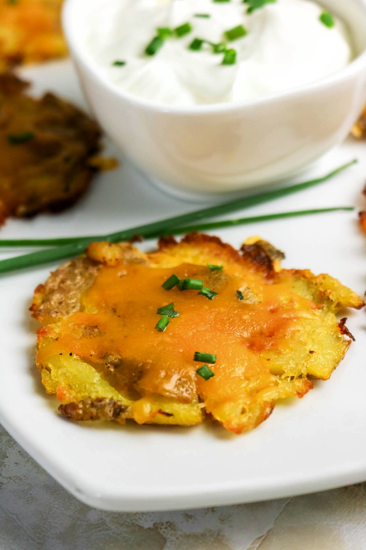 Smashed potato with melted cheese on a serving plate with sour cream on the side.