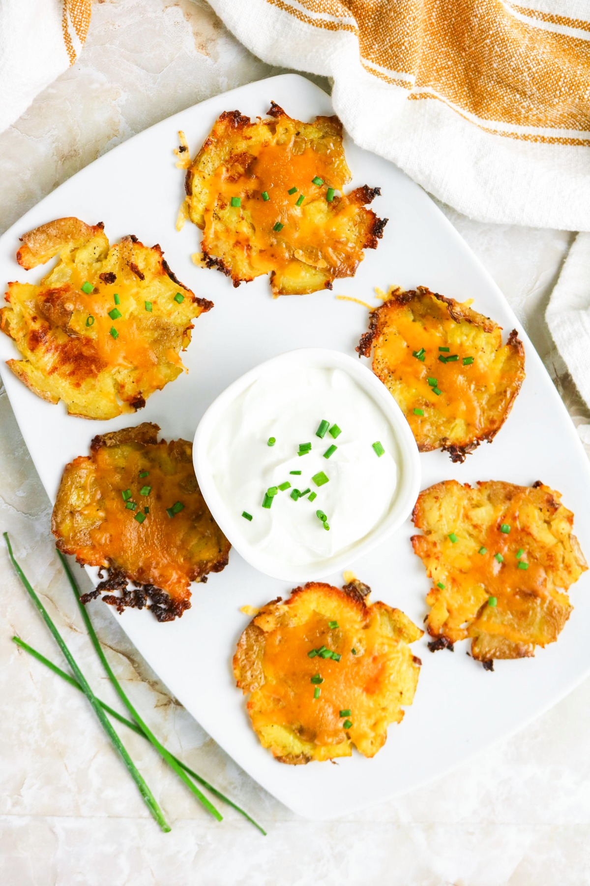 Top view of a white platter with smashed potatoes topped with melted cheese and in a center a bowl of sour cream.