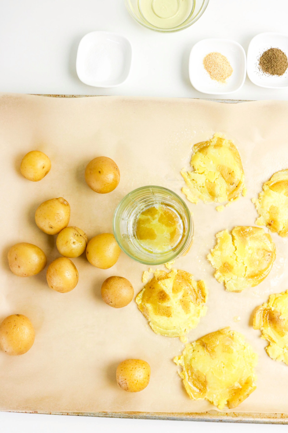 Smashing baby potatoes with a clear glass on top of parchment paper.
