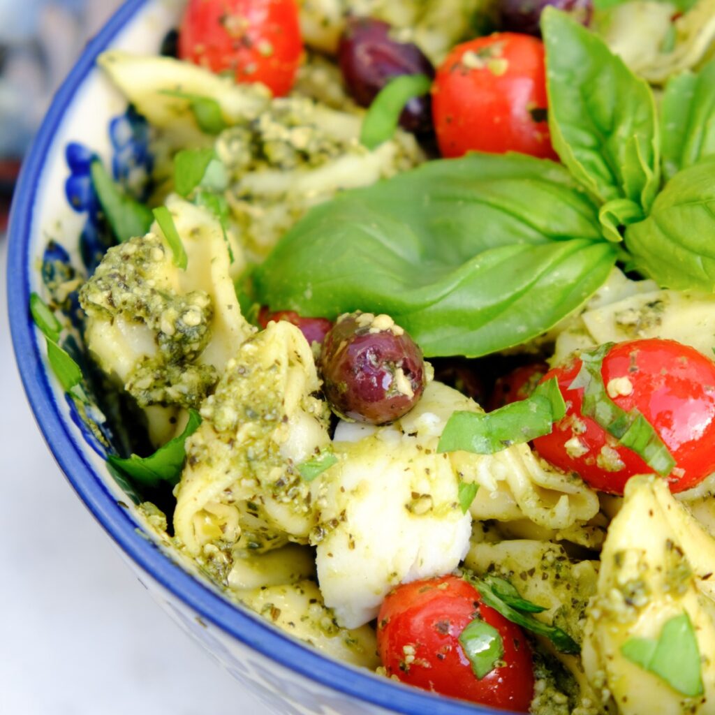 Tortellini pesto salad with basil and tomatoes in a blue serving dish.