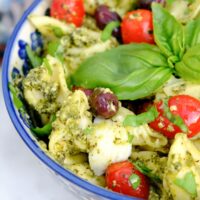 Tortellini pesto salad with basil and tomatoes in a blue serving dish.