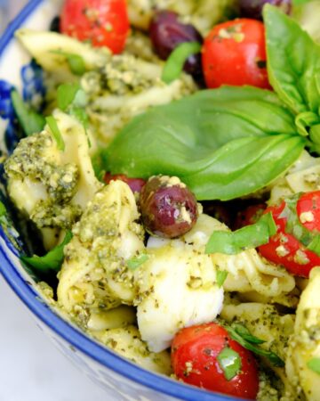 Tortellini pesto salad with basil and tomatoes in a blue serving dish.
